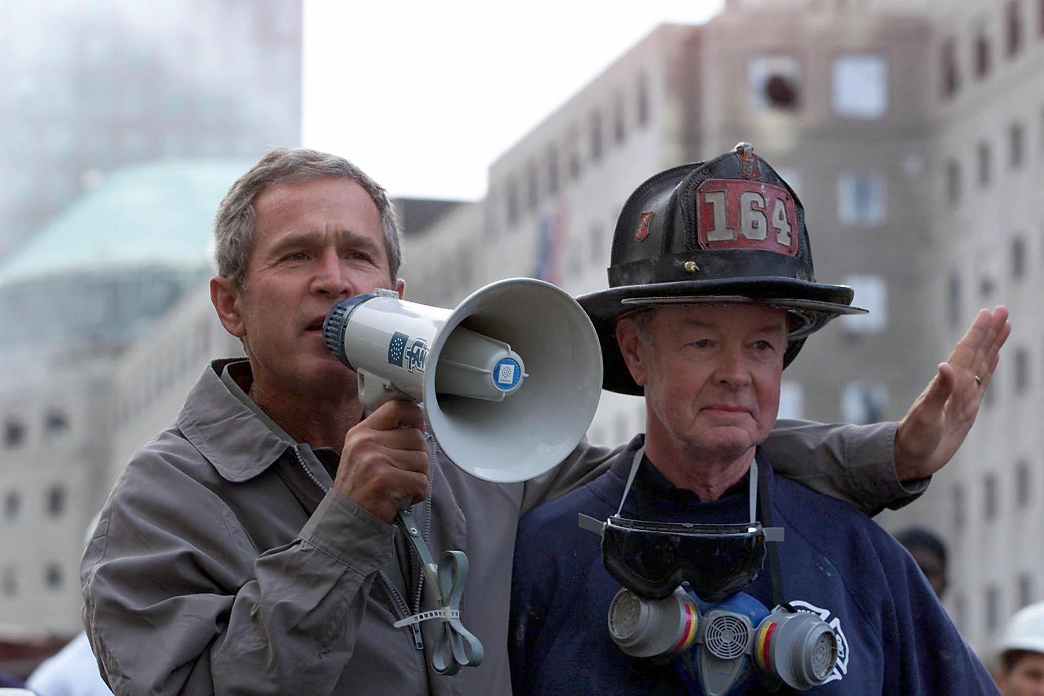 President George W. Bush, left, standing next to retired firefighter Bob Beckwith, 69, speaks to volunteers and firemen as he surveys the damage at the site of the World Trade Center on Sept. 2001 in New York.