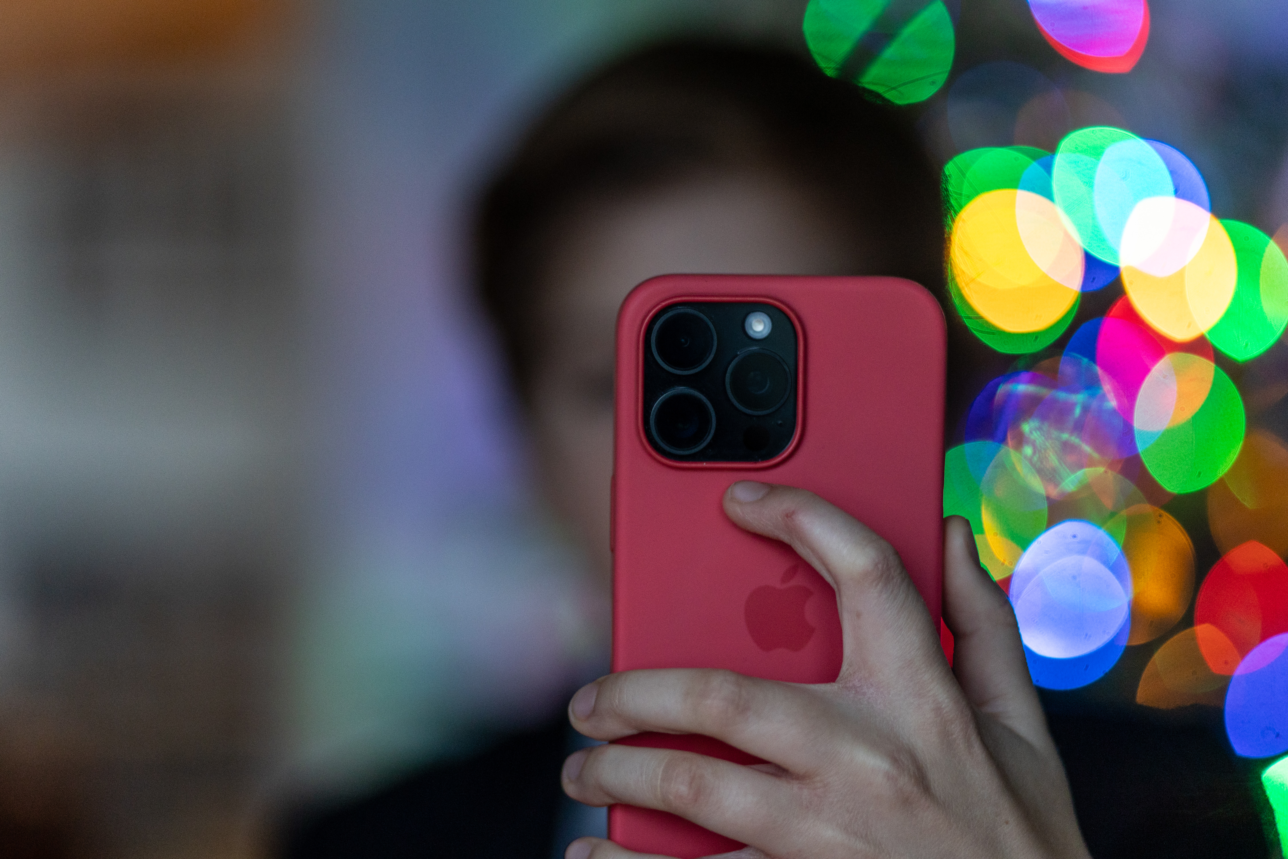 A child whose face is blurred into the background holds up a cell phone.