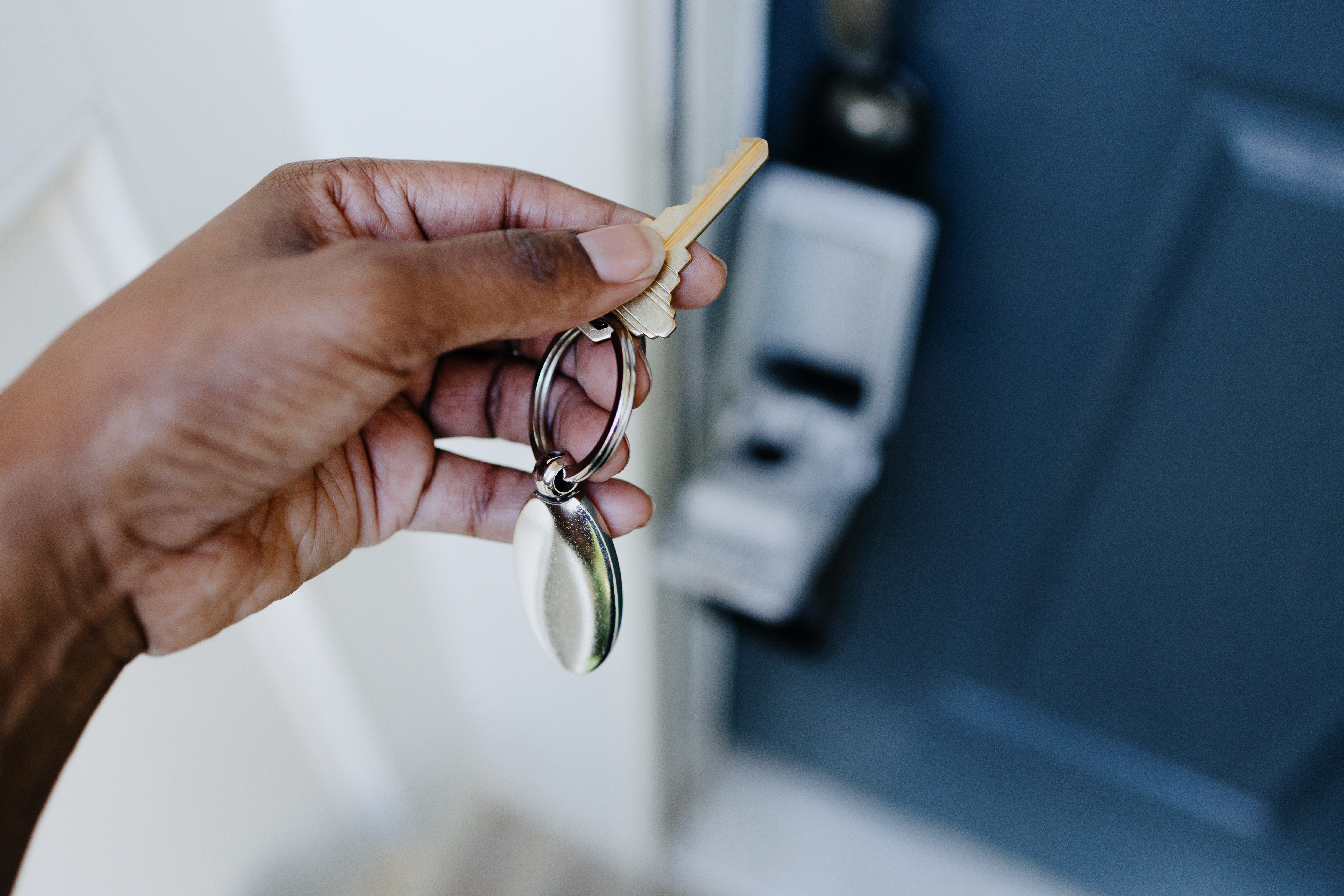 A hand holds a house key in front of a door.