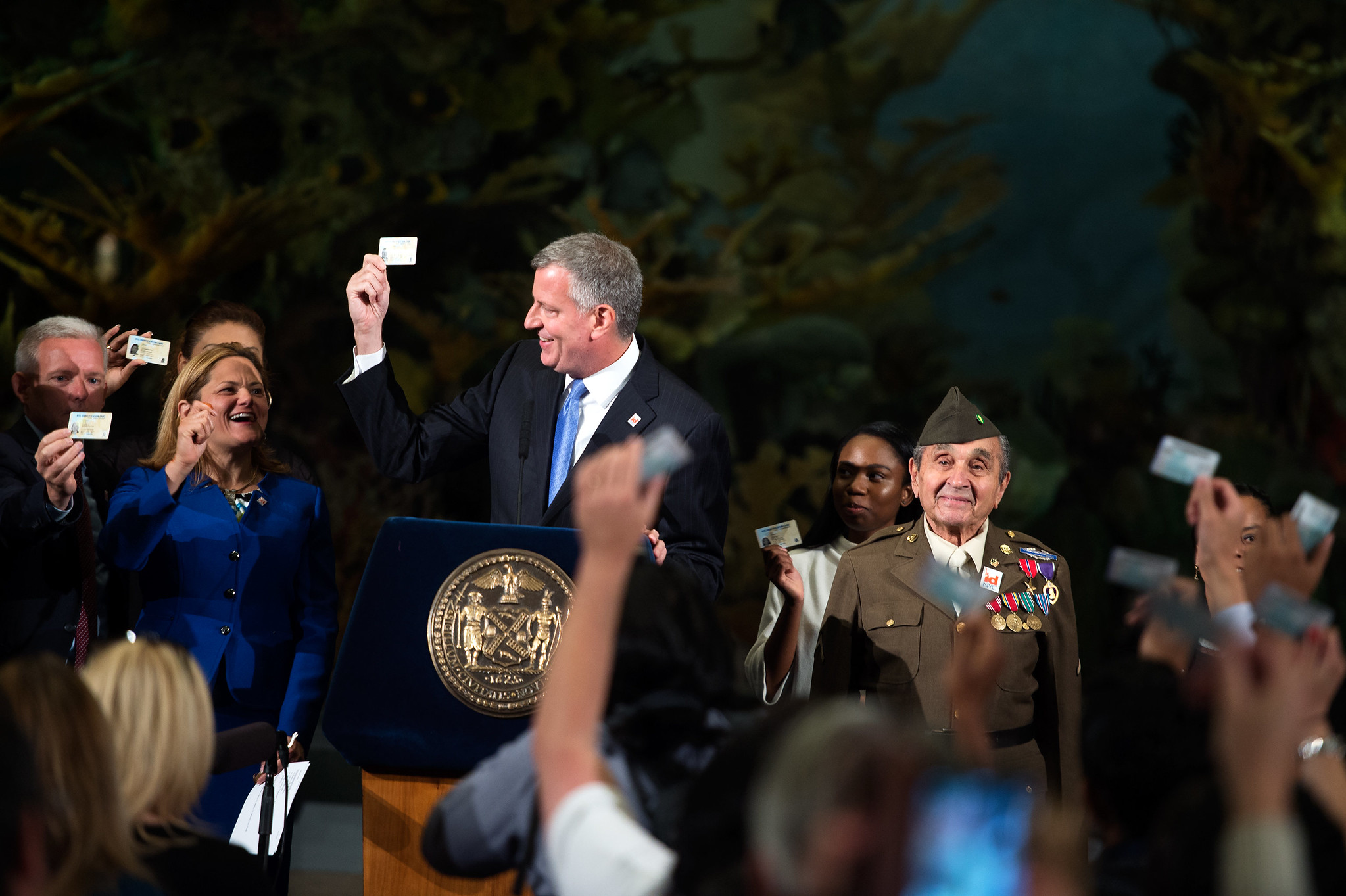 Former Mayor Bill de Blasio holding an IDNYC card as others also display theirs.