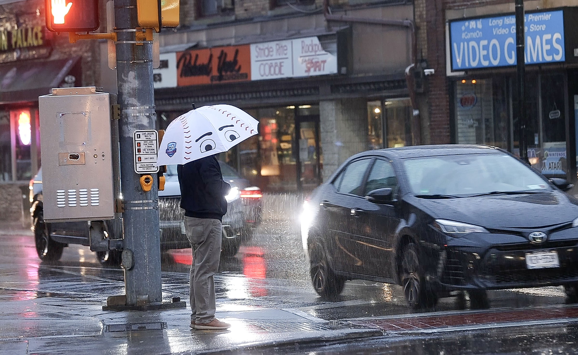 A stock image of someone in the rain on a city street corner.
