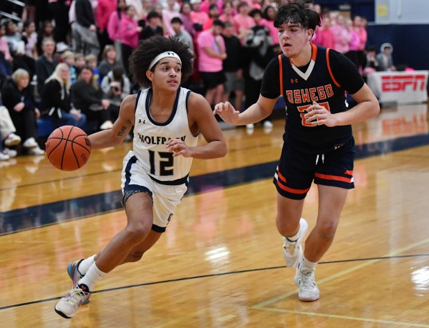 Oswego East's Drey Wisdom (12) drives to score as Oswego's Michael Delgado defends during a game in Oswego on Tuesday, February 13, 2024.(Jon Cunningham for The Beacon-News)