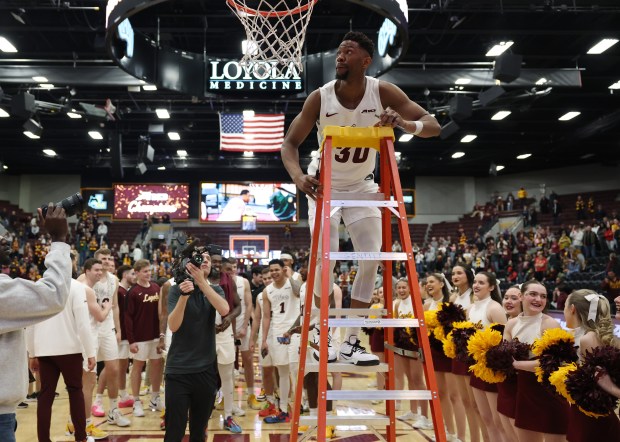 Loyola forward Patrick Mwamba climbs a ladder to cut down a piece of the net after a 64-54 win over La Salle for a share of the Atlantic 10 championship on March 9, 2024, at Gentile Arena. (John J. Kim/Chicago Tribune)