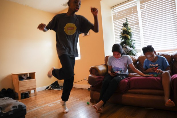 Hezekiah Kelly, runs around as his siblings, Jakayla and Jeremiah, look at phones as they sit on the couch in their apartment in Highland Park on Wednesday, Jan. 3, 2024. (Eileen T. Meslar/Chicago Tribune)