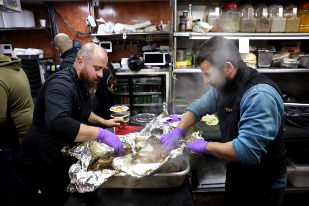 Al Bawadi Grill workers Sagr Al Rawashdeh, left, and Hasan Al Noubani, right, unwrap a lamb roast while preparing for an Iftar at the Bridgeview restaurant during a celebration of Ramadan on Friday, March 15, 2024. (Chris Sweda/Chicago Tribune)