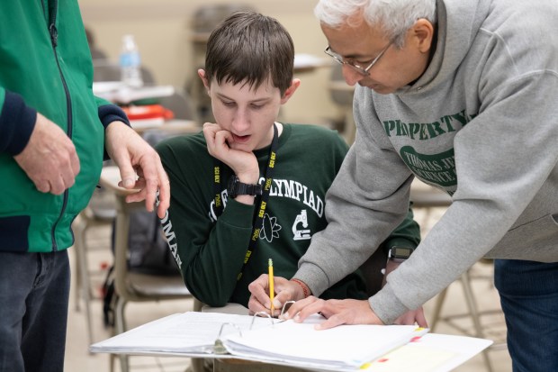 Thomas Jefferson Middle School eighth grader Nathan Allred, center, works on a project involving Planck's constant for optics with coaches, on right, Sunil Dhoot, and Ken Erickson during the Science Olympiad state tournament at Purdue University Northwest in Hammond on Saturday, March 23, 2024. (Kyle Telechan/for the Post-Tribune)