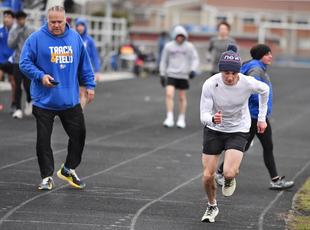 Aurora Central Catholic track coach Troy Kerber starts his timer as runner Patrick Hilby starts a lap during a track team practice, Tuesday, March 26, 2024, in Aurora.(Jon Cunningham/for The Beacon-News)