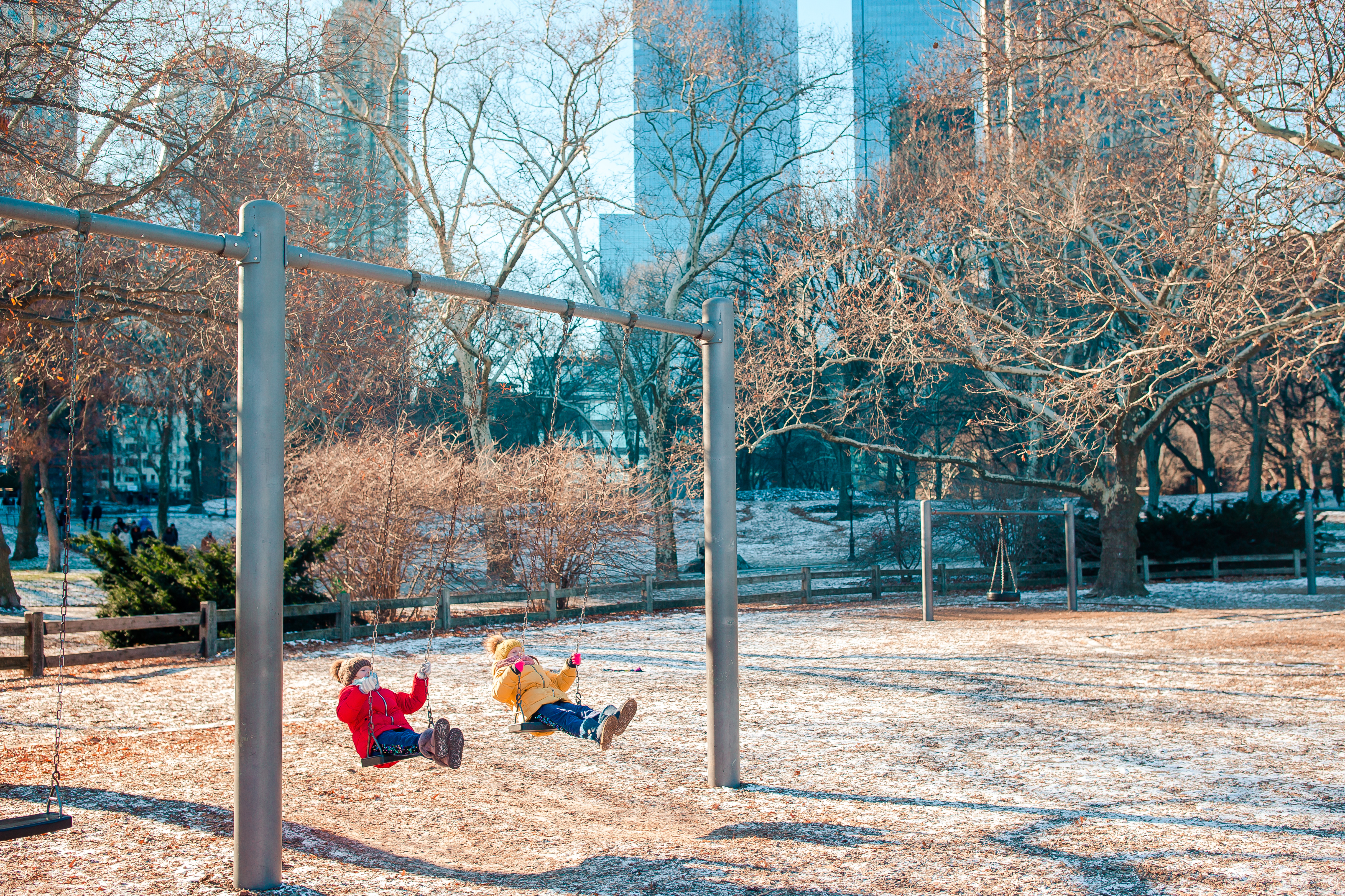 Two young kids on a swing set in a Manhattan park.