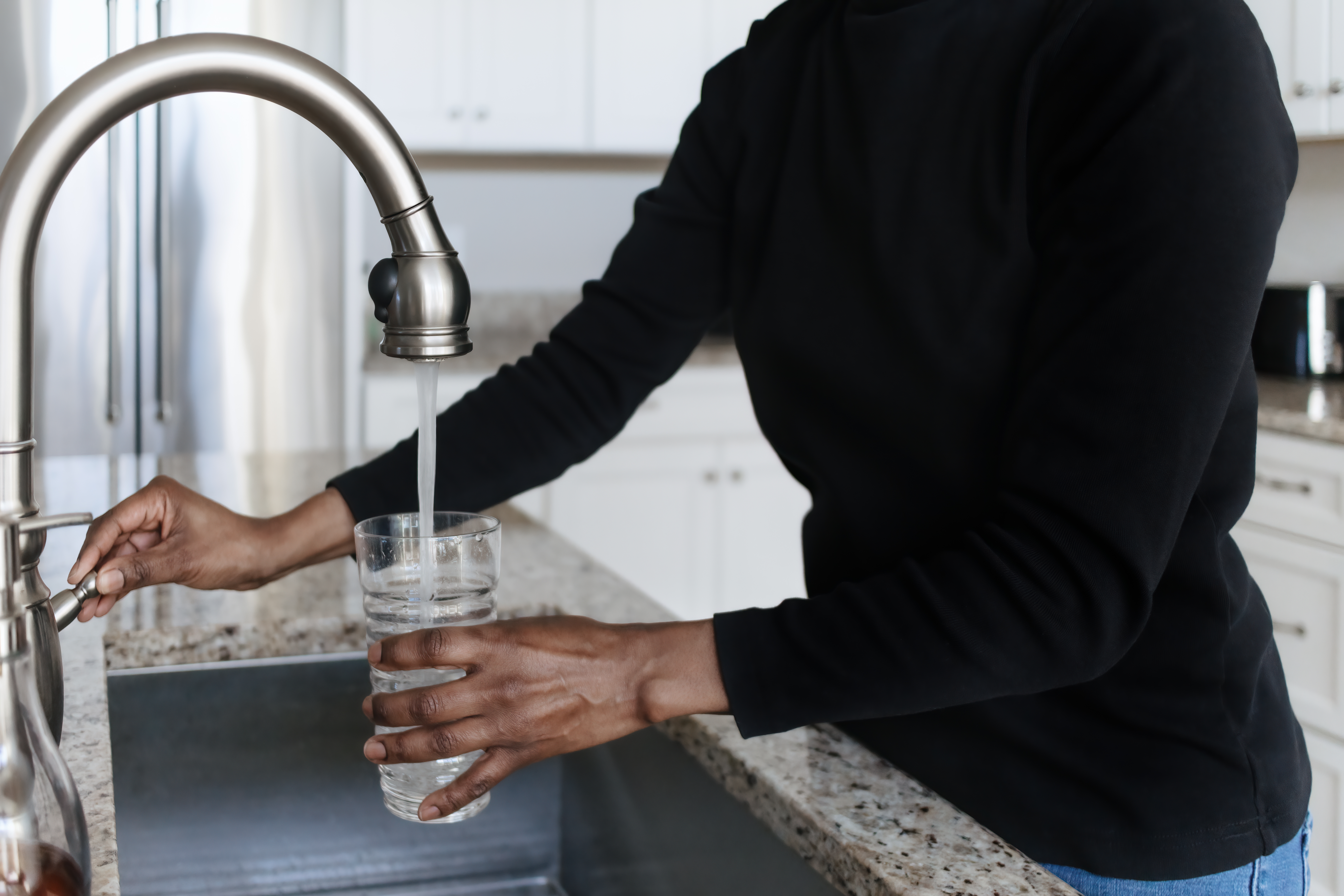 A person fills a water glass from a kitchen sink.