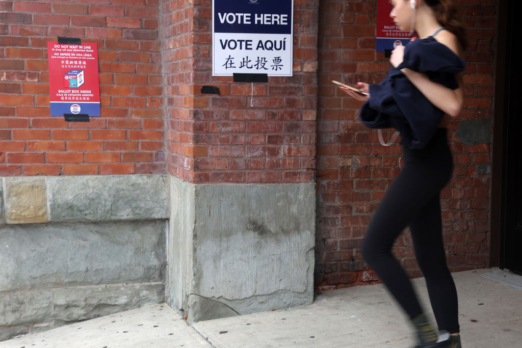 People walk out of a Brooklyn polling place, where signs say "vote here" in several languanges.