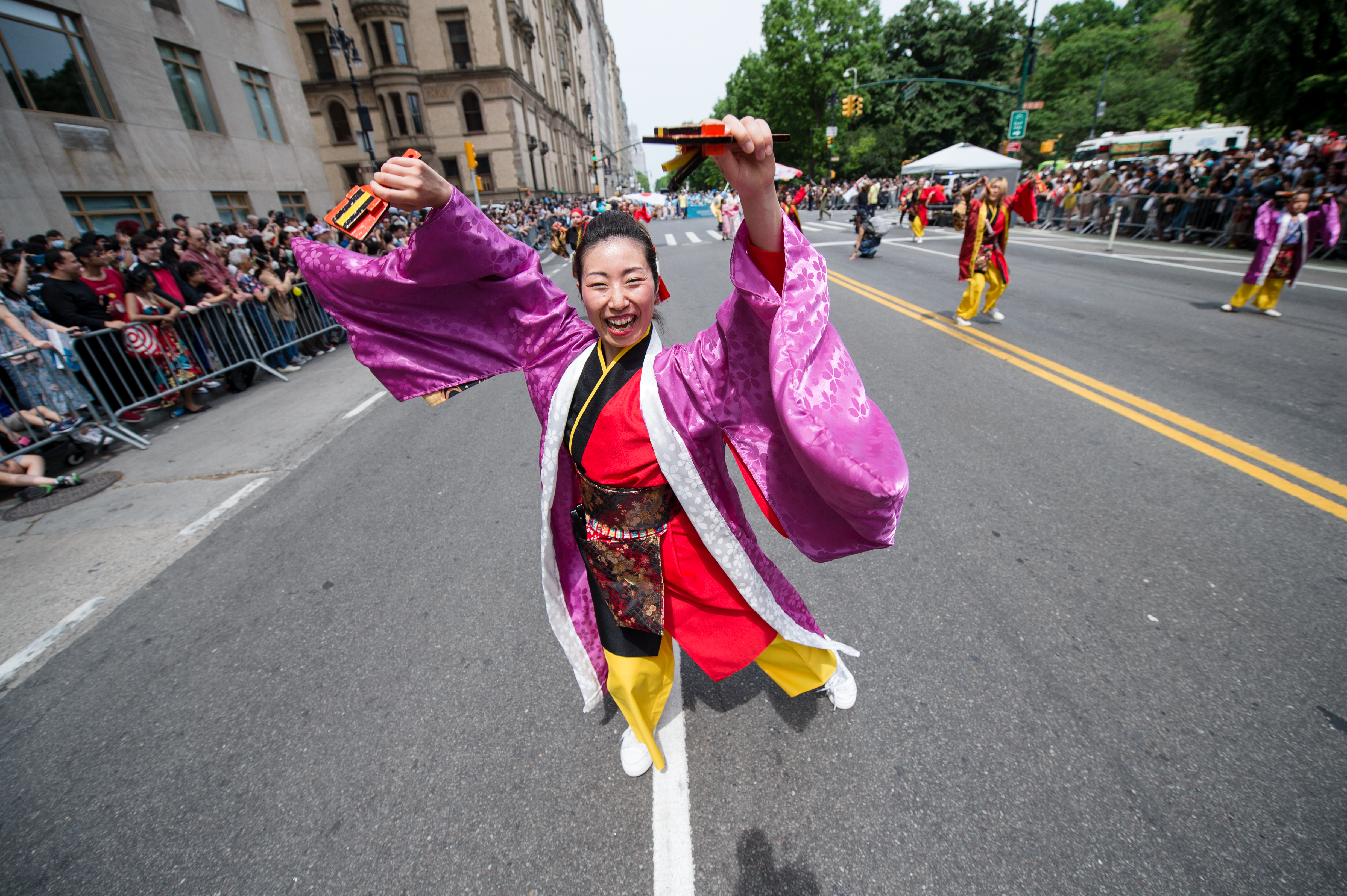 a woman wearing purple dances down a street for a parade.