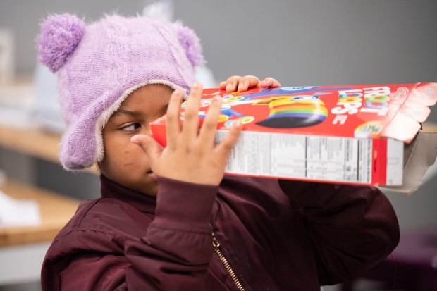 Gary Resident Kaylee Glover, 7, peers through a cereal box fashioned into an eclipse-viewing device during a program at the Gary Public Library on Saturday, March 23, 2024. (Kyle Telechan/for the Post-Tribune)
