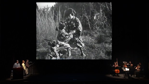 An image from a 2019 UCLA presentation of "The Art of the Benshi," with orators on the left, musicians on the right and a silent film presentation center stage. (UCLA)