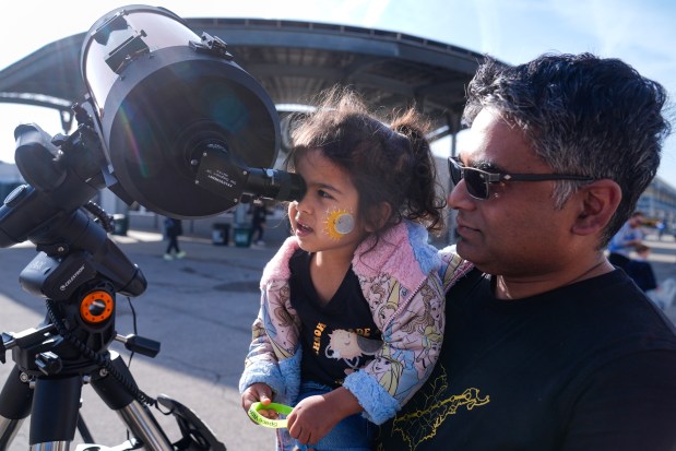 Tawhid Rana, of Midland, Mich., hold his daughter Thia, as she views the sun through a telescope at the Indianapolis Motor Speedway in Indianapolis, Monday, April 8, 2024. (AP Photo/Michael Conroy)