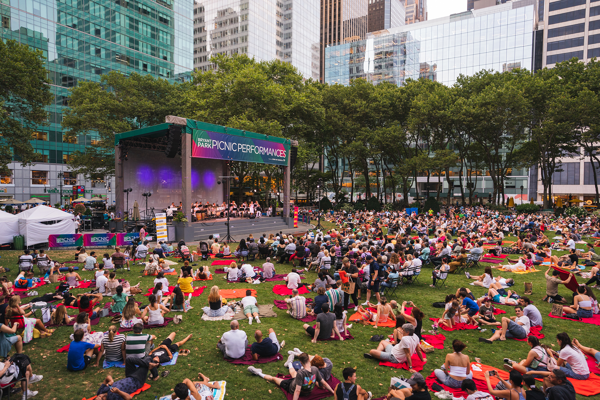 A group of people sit on a lawn for a concert.