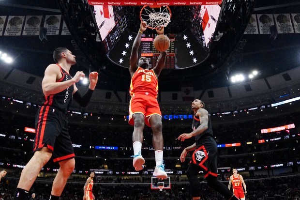 Atlanta Hawks center Clint Capela, center, hangs from the rim after dunking as Chicago Bulls center Nikola Vucevic, left, and forward DeMar DeRozan look on during the first half of an NBA basketball game in Chicago, Monday, April 1, 2024. (AP Photo/Nam Y. Huh)