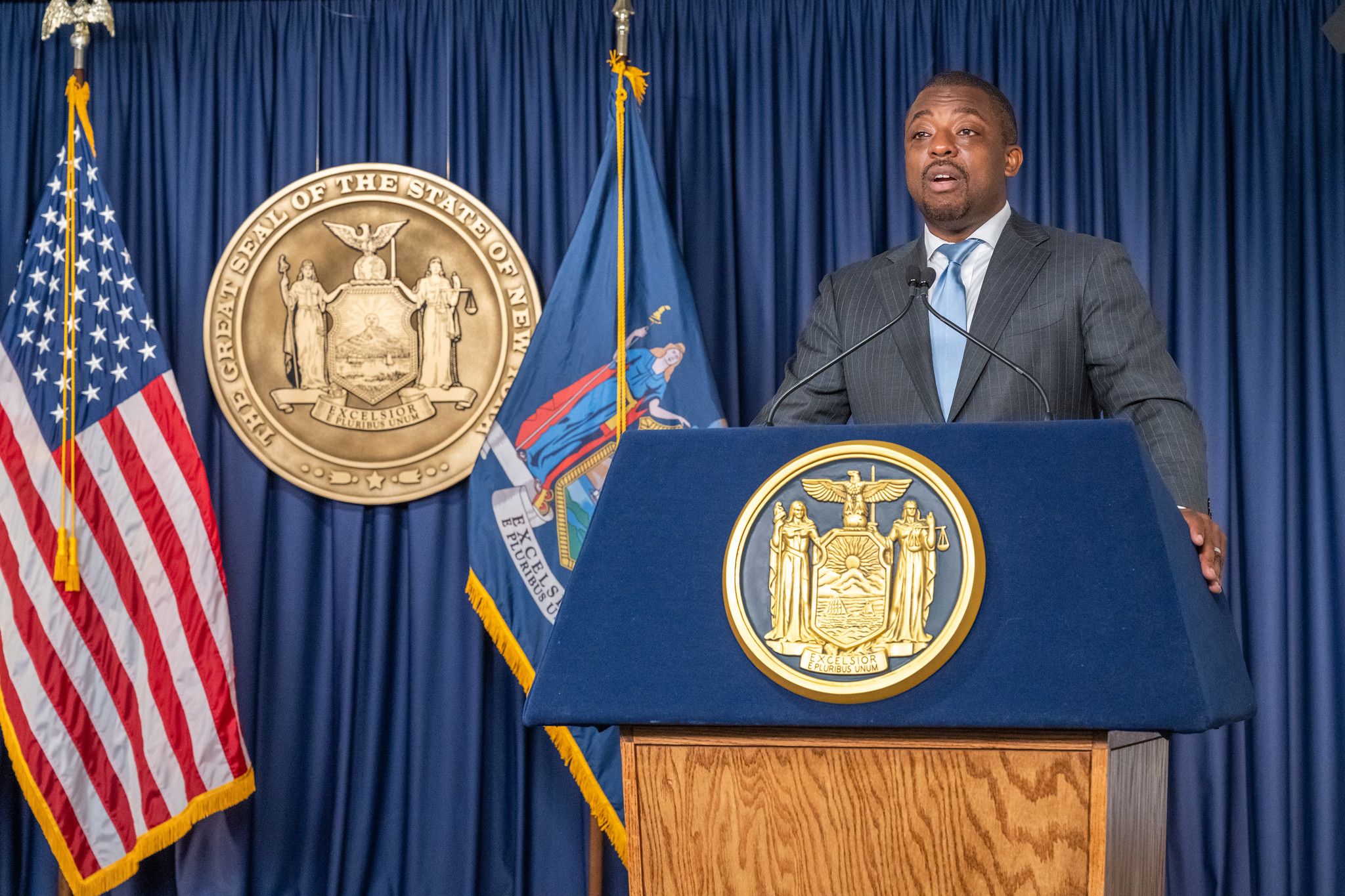 Then-Lt. Gov. Brian Benjamin speaks at a podium with the state seal, the American flag and New York state flag draped in the background.