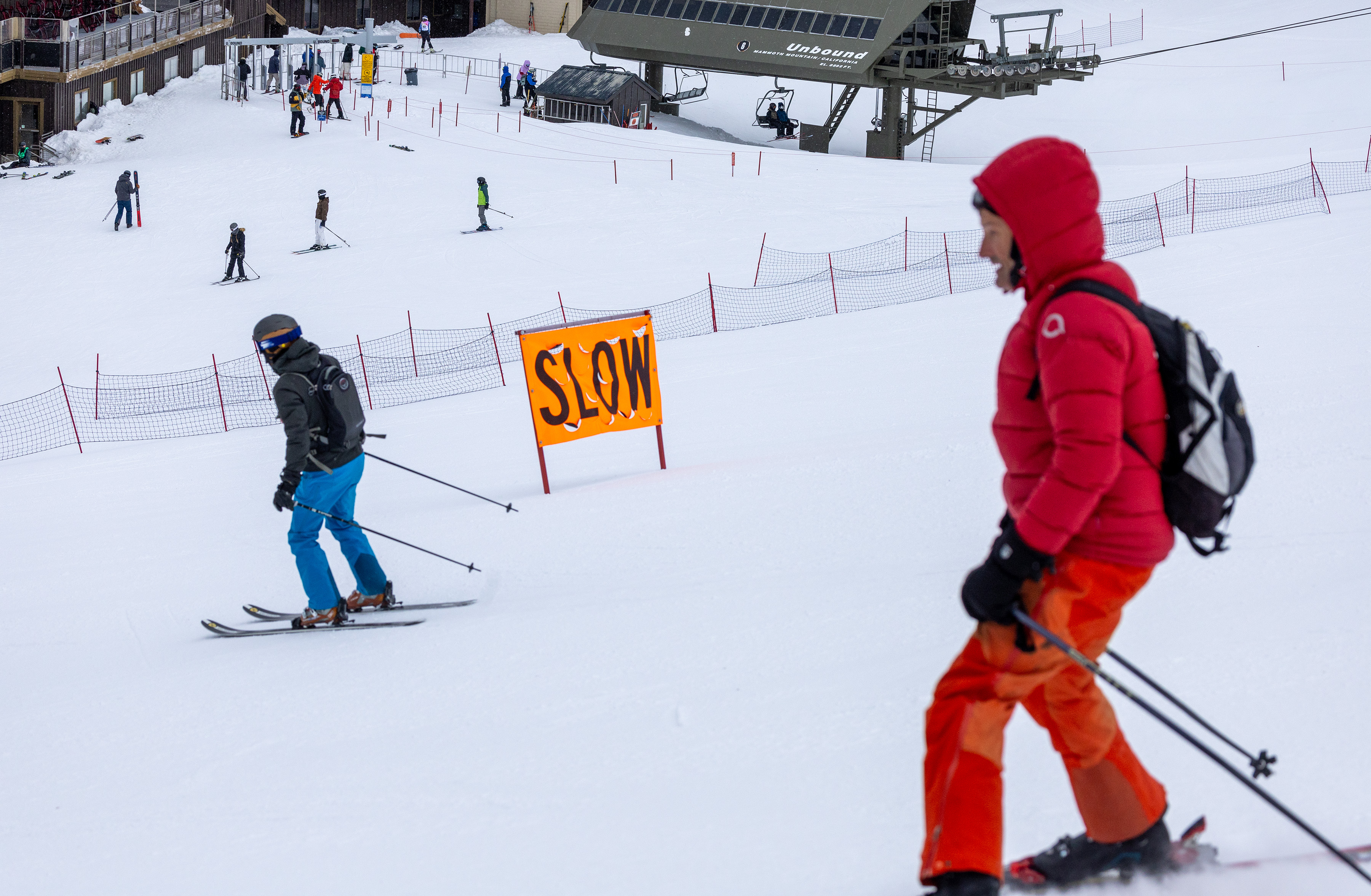 skiers on a mountain pass a "slow" sign