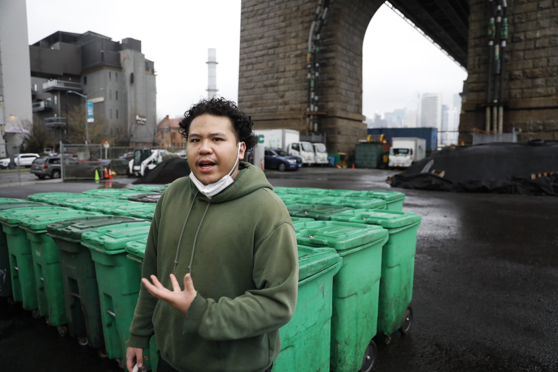 A man in a hoodie stands in front of compost bins beneath the Queensboro Bridge.