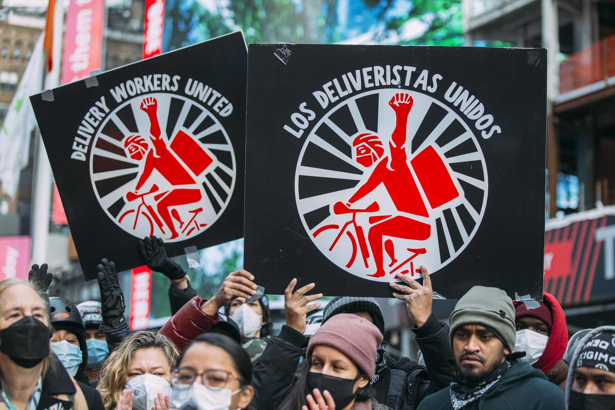 Demonstrators hold "Los Deliverista Unidos" signs, which show a red cartoon delivery worker.