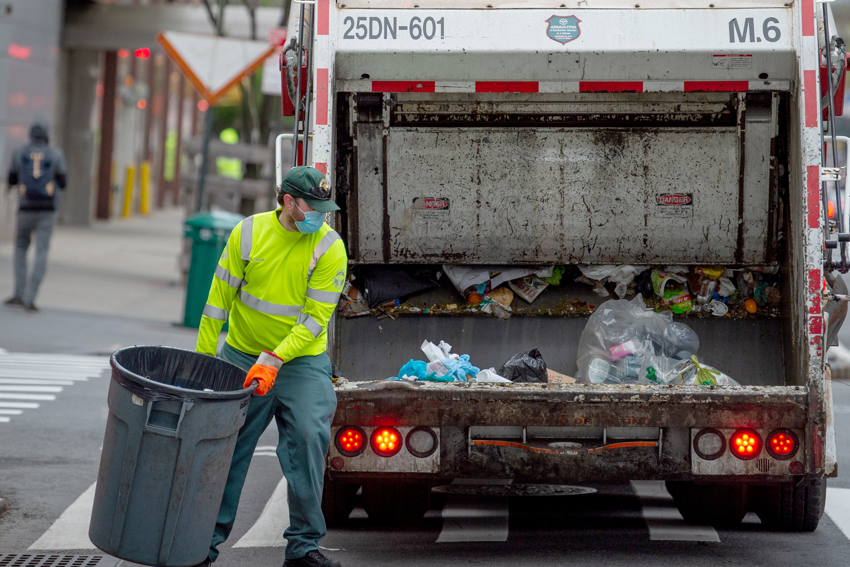 A New York City Department of Sanitation worker wearing a mask and gloves collects the trash.