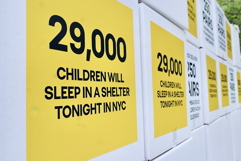 A yellow poster says "29,000 children will sleep in a shelter tonight in NYC/"