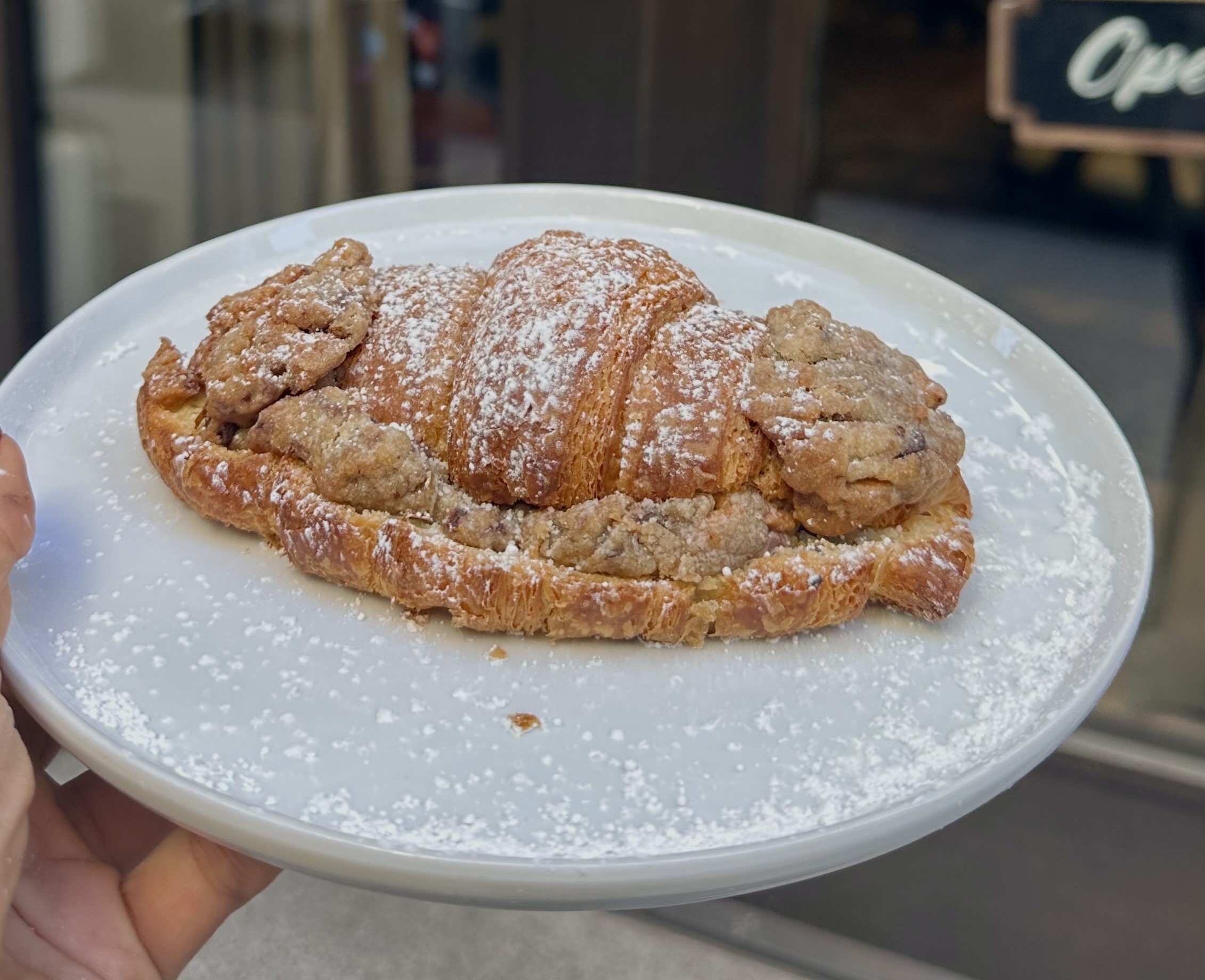 a person holds a white plate with a croissant-cookie hybrid