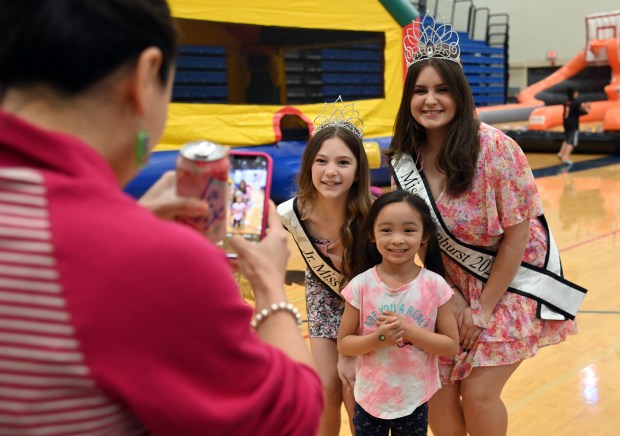 Left, parent Emily Penn of Lindenhurst takes a photo of daughter Lily, 5, a kindergartner, photographed with Lindenhurst royalty, from left, top row, Jr. Miss Lindenhurst 2023 Ivy Catania, 12, a seventh-grader from Lindenhurst and Miss Lindenhurst 2023 Danika Huff, 16, a junior at Lakes Community High School at the Spring Fest Expo at Lakes Community High School in Lake Villa on April 6, 2024. (Karie Angell Luc/Lake County News-Sun)