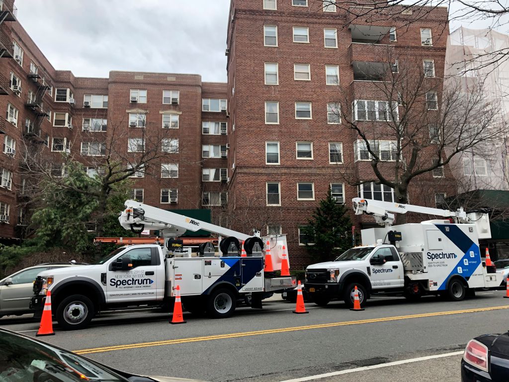 Two Spectrum internet trucks parked outside of a building in Queens.