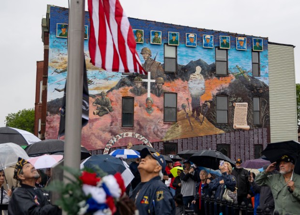 Veterans raise a flag in front of the large mural on May 26, 2024, during a Memorial Day event in South Chicago near Our Lady of Guadalupe Church to honor 12 men from the community who died in the Vietnam War. A fundraising effort is underway to restore the mural. (Brian Cassella/Chicago Tribune)
