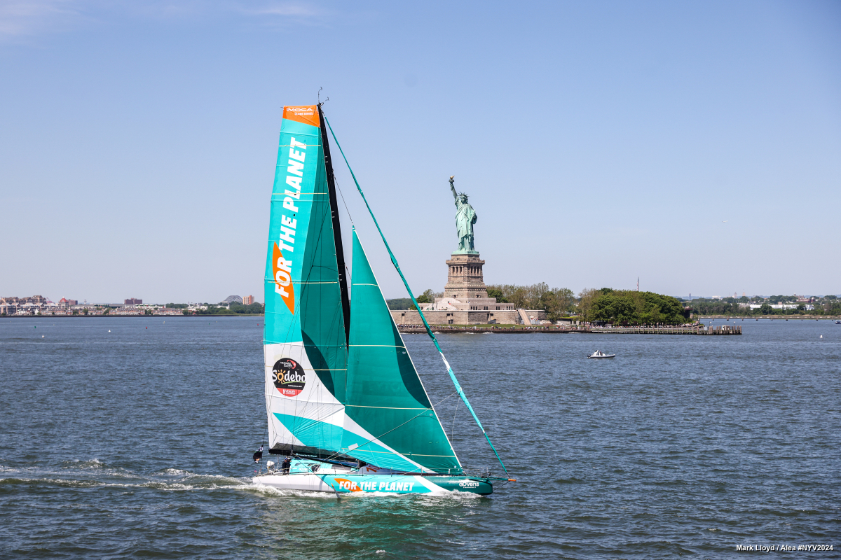 A sailboat pictured in the water with the Statue of Liberty in the background.