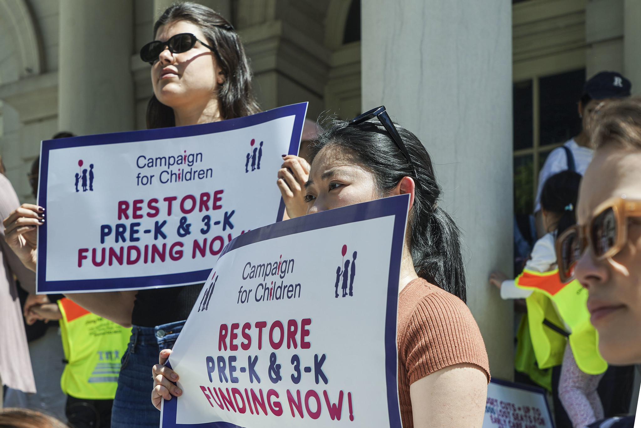 A child and adult hold signs calling for the restoration of early childhood education funding.