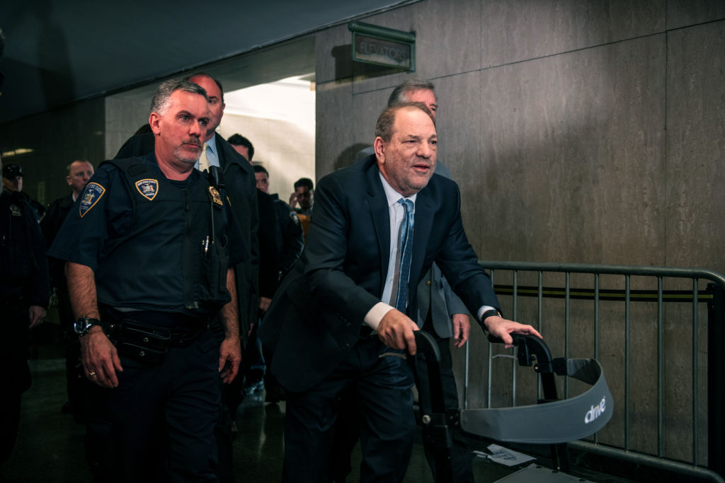 Film producer Harvey Weinstein walks through the hallway of Manhattan criminal court, escorted by an officer.