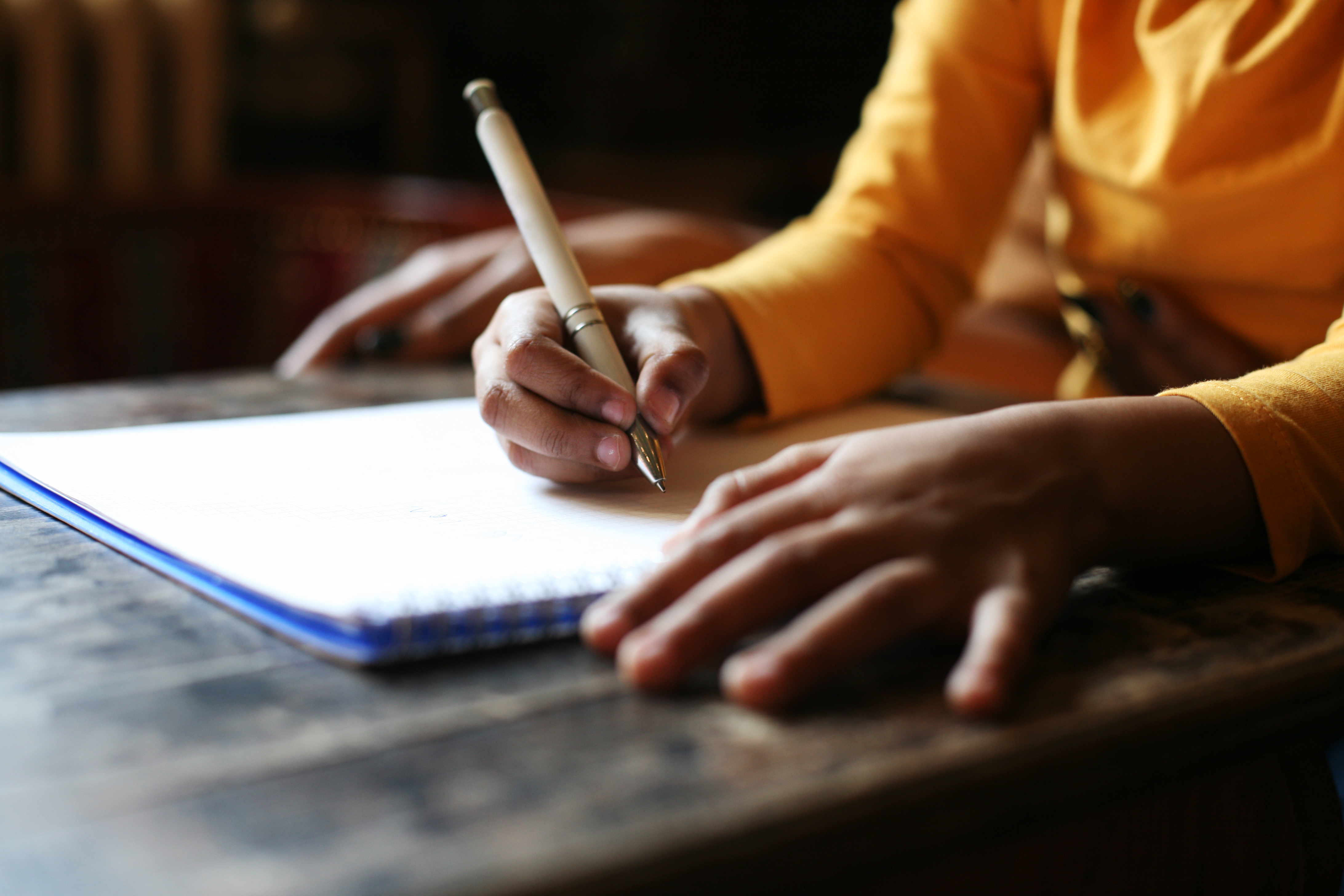 A stock image of a student writing at a school desk.