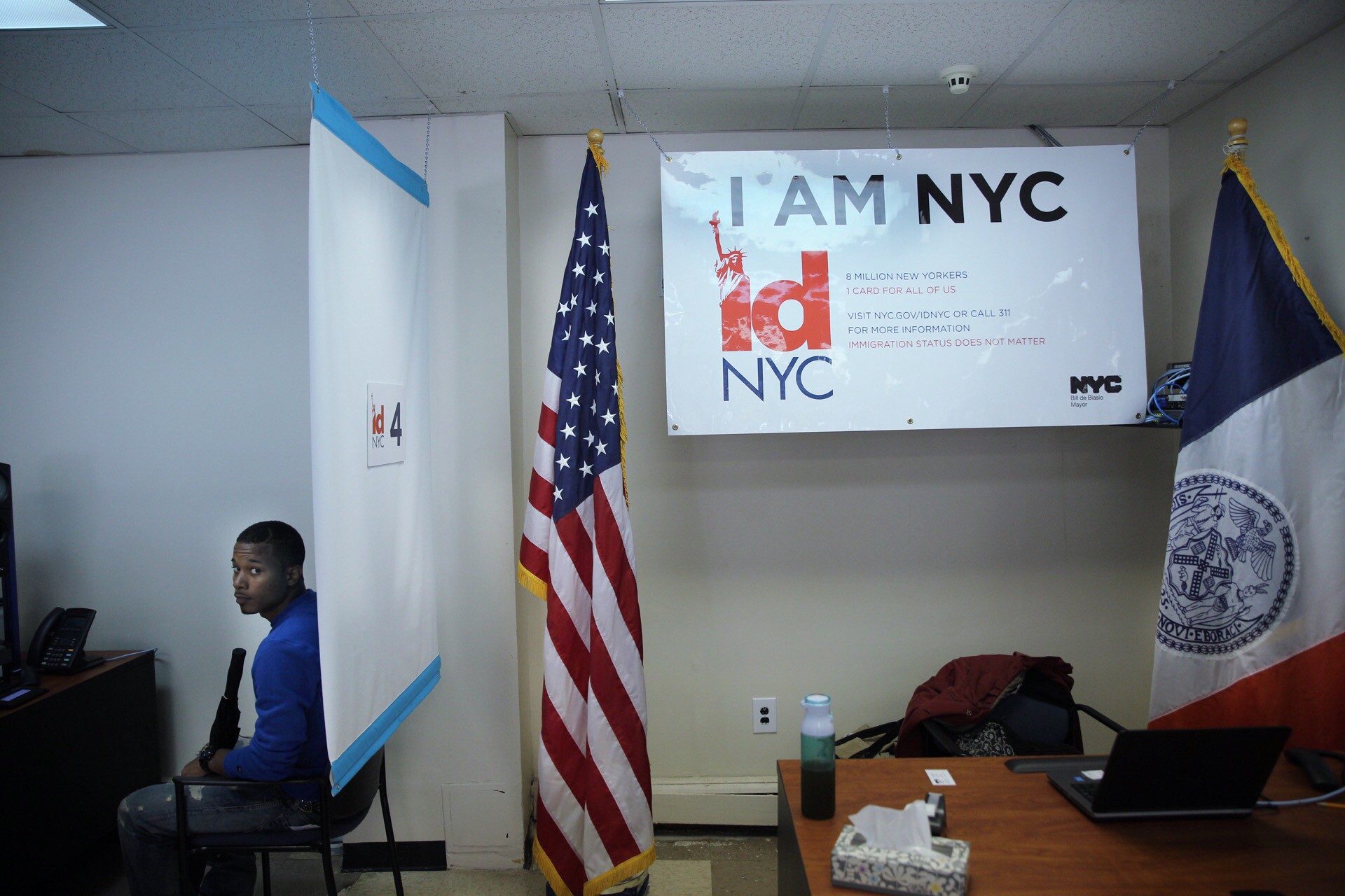 A person sits in front a white screen waiting for their picture to be taken for an IDNYC card.