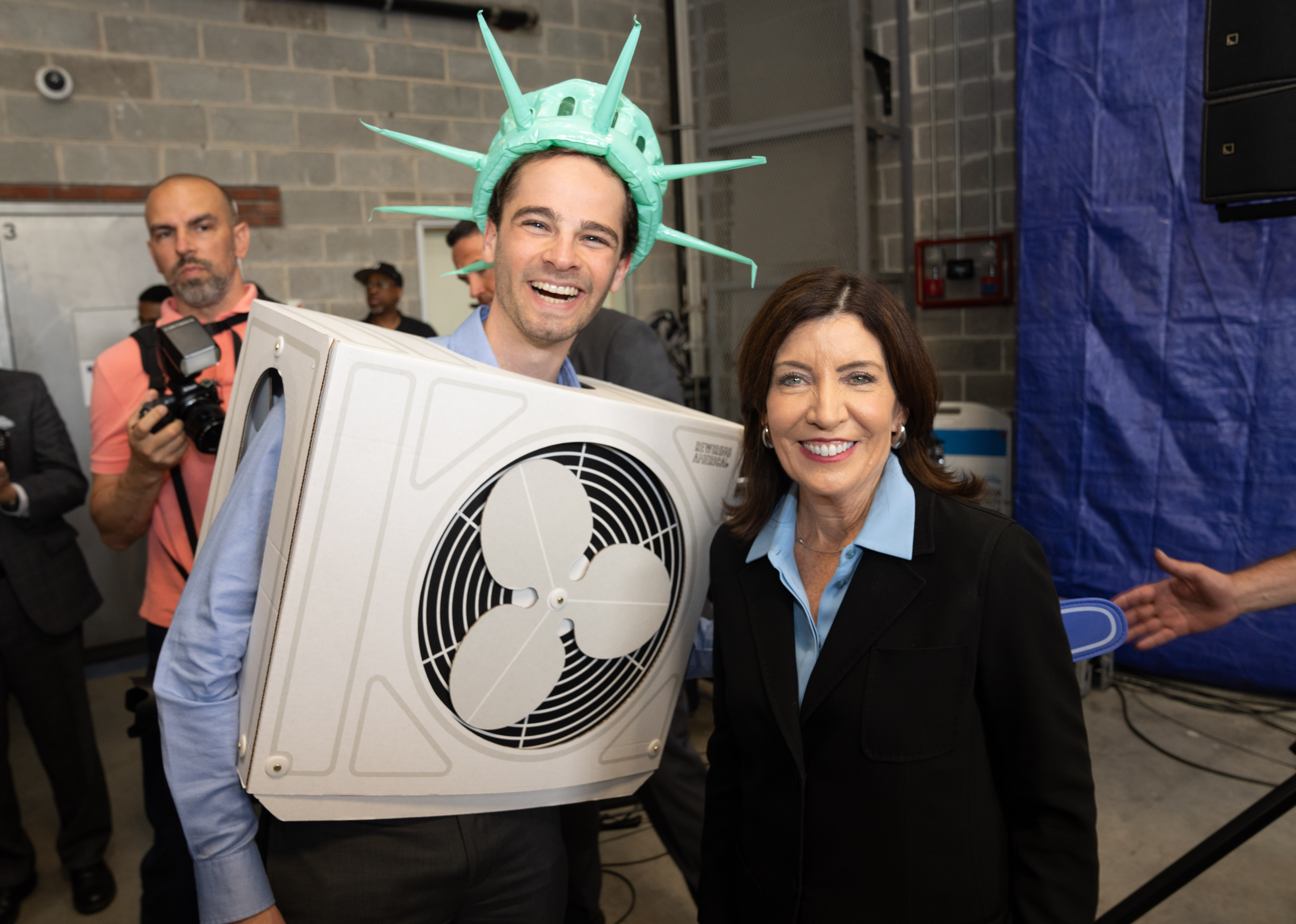 Gov. Kathy Hochul smiles with a man in a silly heat pump costume.