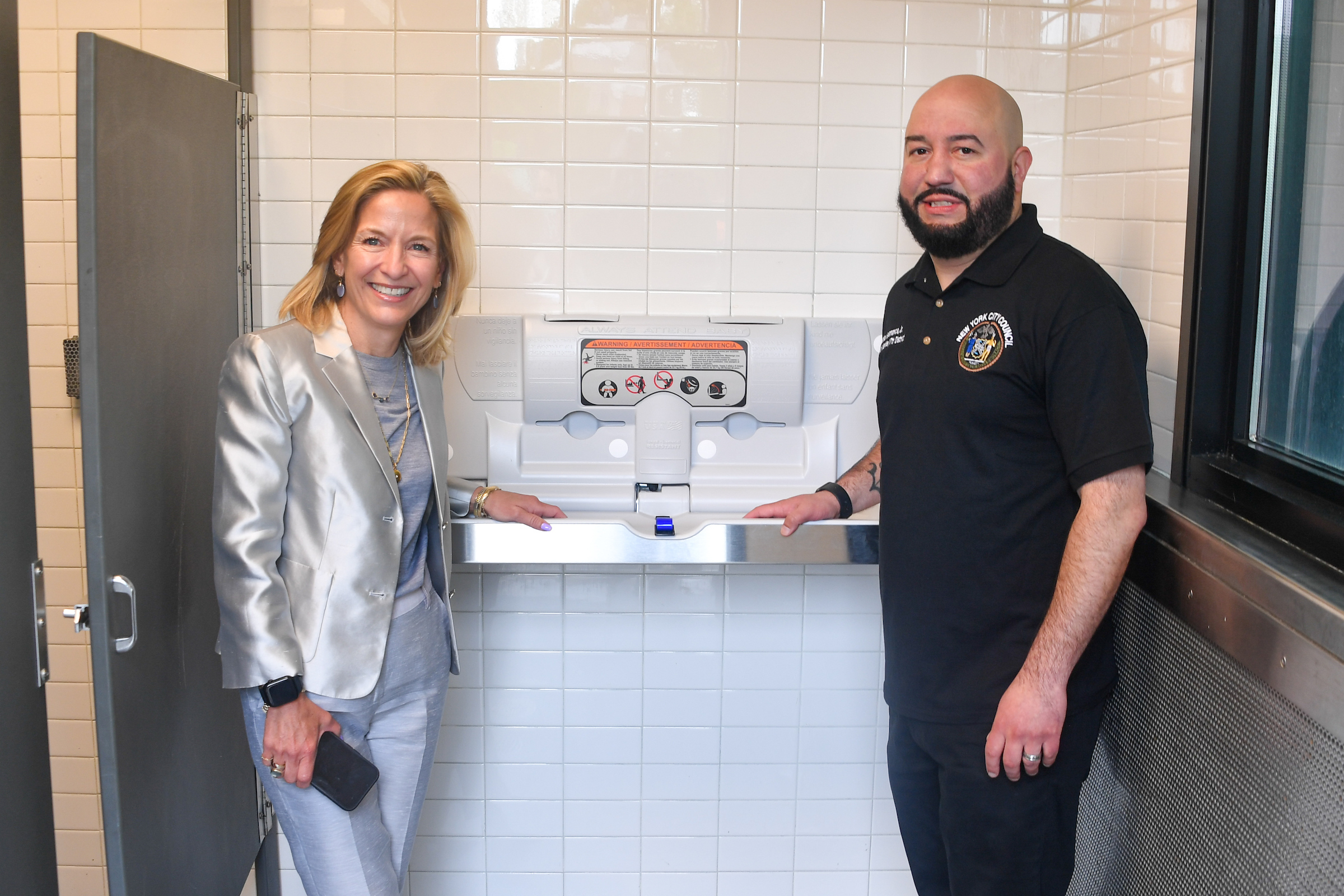 A man and woman standing in a bathroom near a changing table.