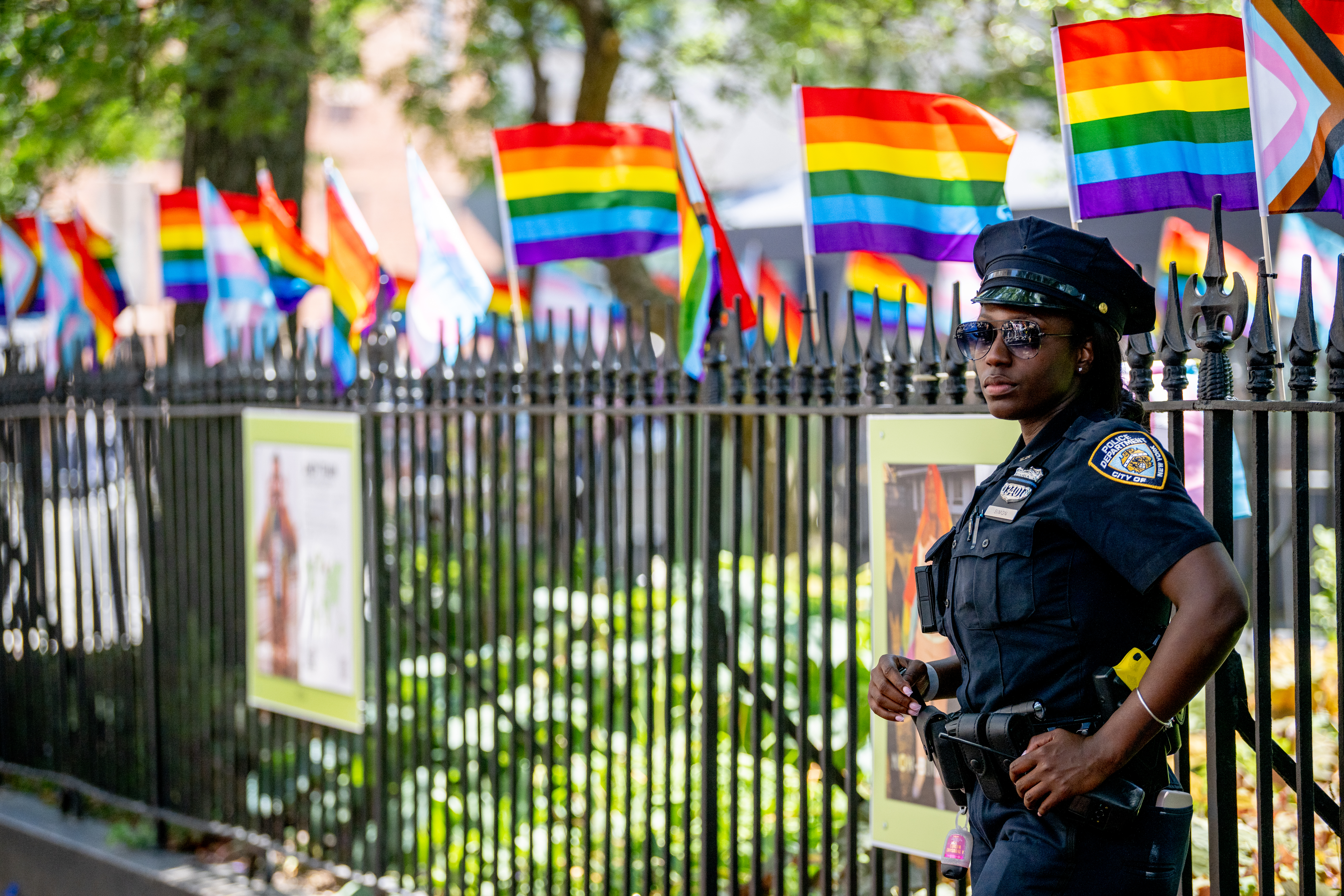 A female police officer stands by a gate decorated with gay and trans pride flags.