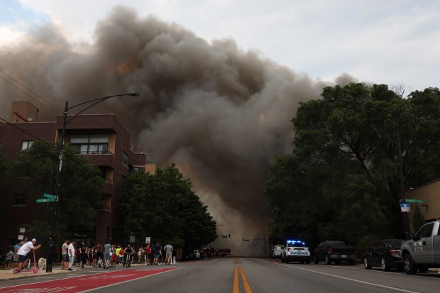 People watch from West Chicago Avenue as a building burns in the 2800 block of West Grand Avenue in Chicago on Wednesday, June 19, 2024. The fire was raised to a 3-11 alarm by about 7:15 p.m. (John J. Kim/Chicago Tribune)