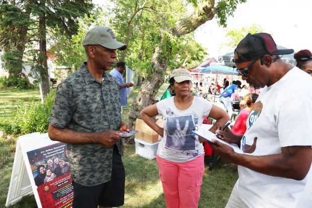 Howard Ray's father, Howard Ray Sr., left, and his wife, Mary, get a signature from Laighton Scott, of Maywood, on June 19, 2024, in Hillside on a petition to put a reparations referendum on the ballot. (Terrence Antonio James/Chicago Tribune)