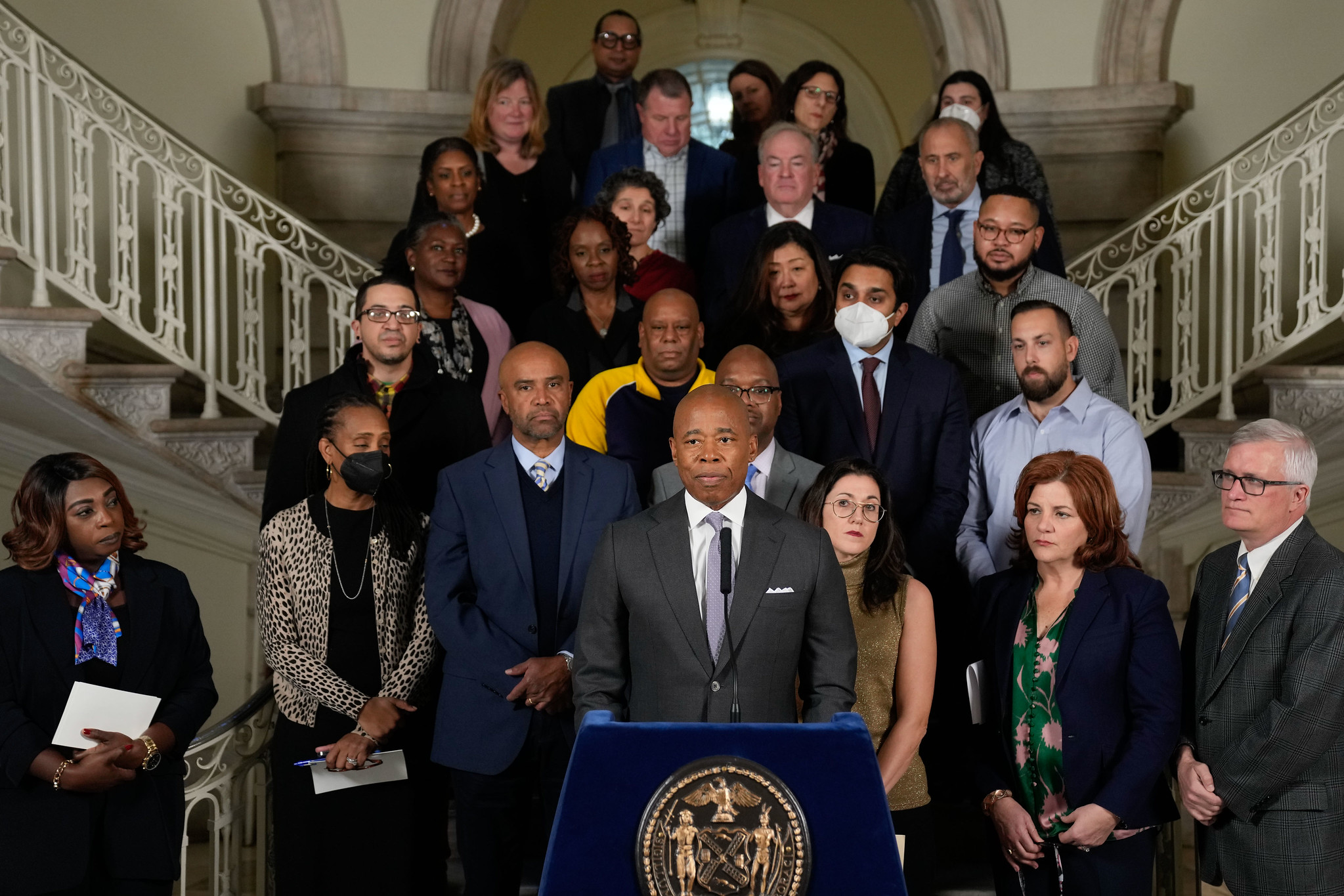 Mayor Eric Adams, flanked by lawmakers, shelter providers and top housing officials, stand together inside of City Hall.