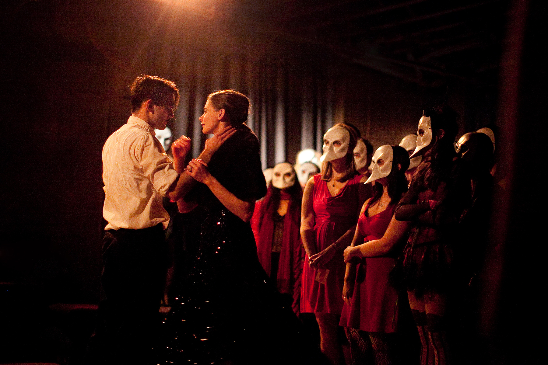 Two people caress in a theater while onloookers stand by in masks.