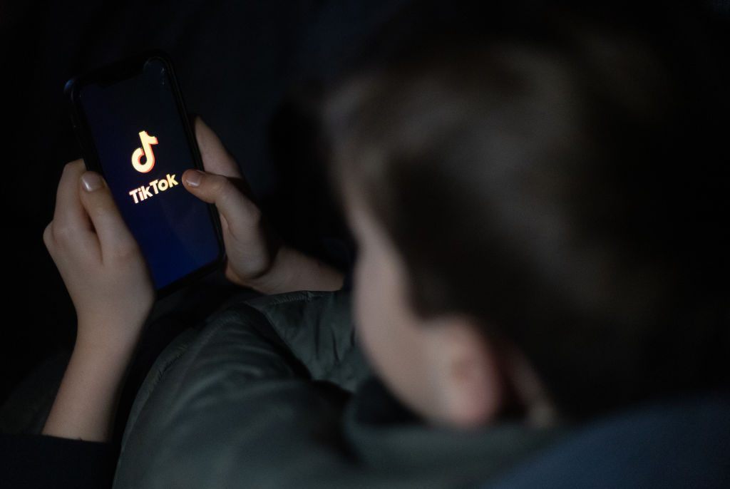 A young boy looks at his phone screen displaying the TikTok logo.