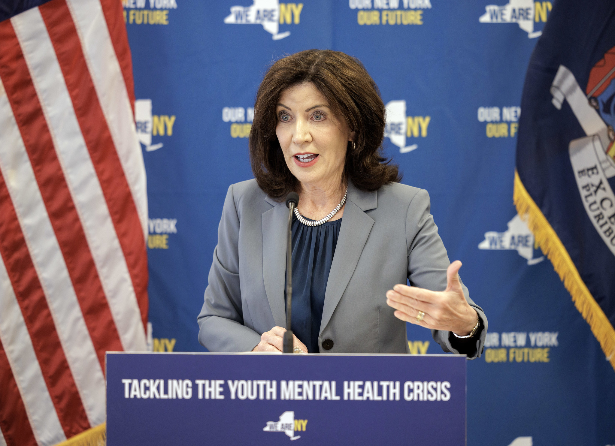 Gov. Kathy Hochul stands behind a podium fixed with a sign that says "tackling the youth mental health crisis."