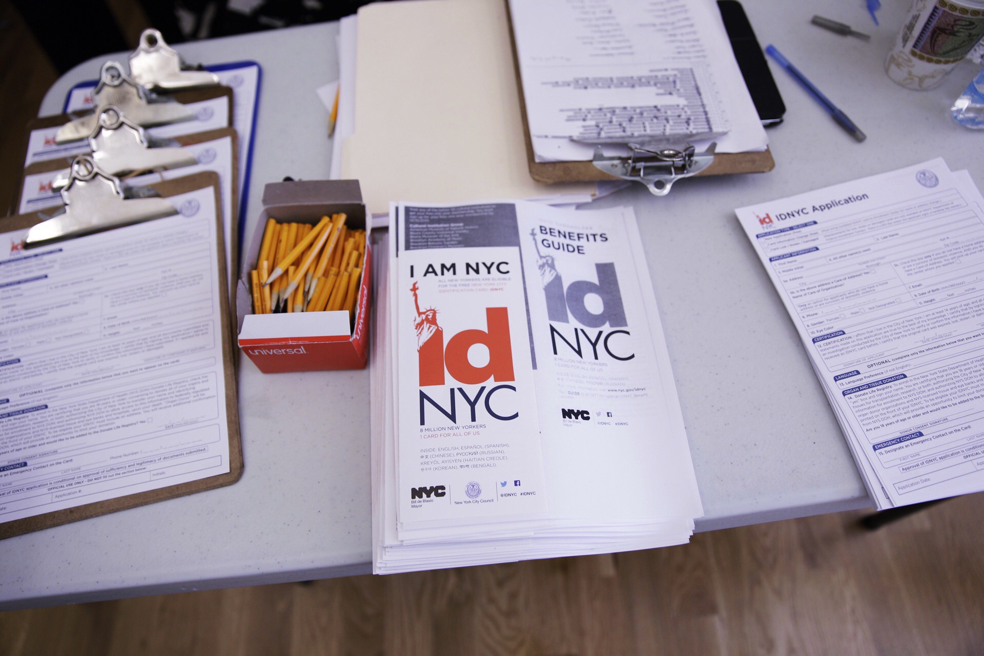 IDNYC pamphlets and forms are laid out on a table, along with pens and pencils.