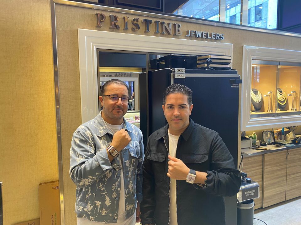 Two men pose in front of a jewelry store.