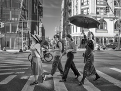 Woman with an umbrella on a sunny day crossing Mercer Street at Houston Street in Manhattan.
