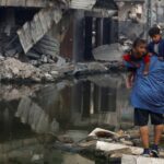 A Palestinian man holds his children as he walks next to buildings destroyed in an Israeli strike, in Khan Younis